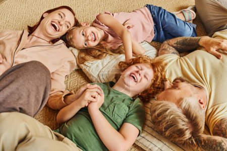 Ansicht von lachenden Eltern und Kindern im Liegen und auf dem Boden, die sich im modernen Wohnzimmer vergnügen