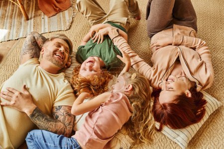 vista superior de los padres emocionados y los niños que se divierten en el suelo en la sala de estar moderna, momentos apreciados