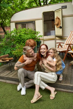 Foto de Niños emocionados abrazando a padres riendo sentados en casa remolque al aire libre, momentos de unión - Imagen libre de derechos