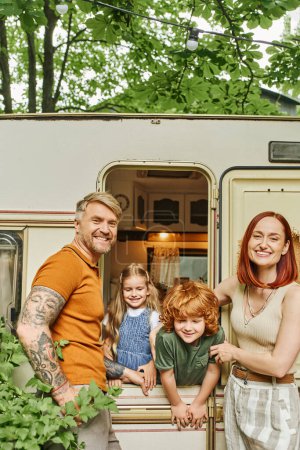 Photo for Cheerful couple smiling at camera near kids having fun in trailer home, family quality time - Royalty Free Image