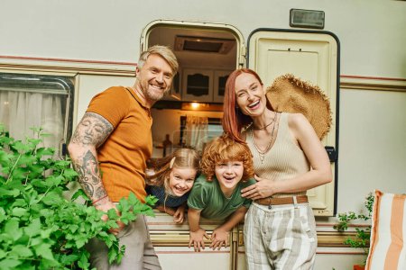 Photo for Laughing couple looking at camera near kids having fun in trailer home, adventure and relaxation - Royalty Free Image