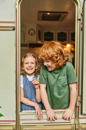 adorable and cheerful brother and sister laughing inside trailer home, siblings relationship