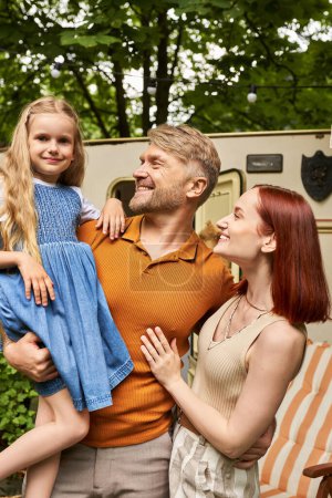 Photo for Joyful man holding cute daughter near happy wife and mobile home in trailer park, leisure together - Royalty Free Image