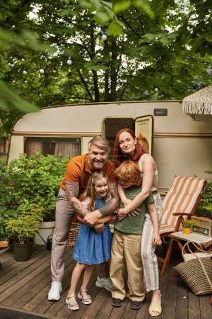 Photo for Happy parents embracing cheerful children near modern home on wheels in trailer park, family leisure - Royalty Free Image