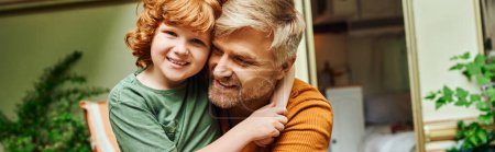 Téléchargez les photos : Joyeux rousse garçon embrassant père heureux et regardant la caméra près de la maison de remorque, bannière horizontale - en image libre de droit