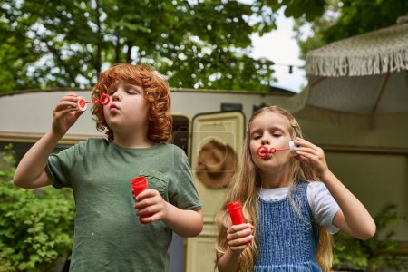 Photo for Redhead brother and blonde sister blowing soap bubbles near trailer home, siblings relationship - Royalty Free Image