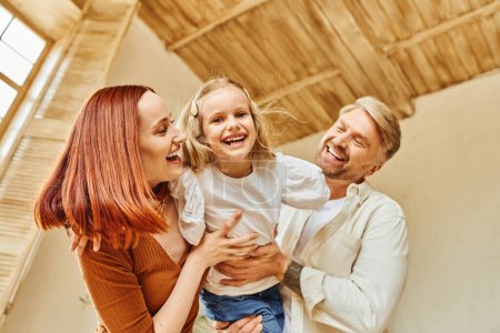 happy parents playing with overjoyed daughter in living room at cozy home, bonding moments