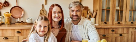 smiling parents with adorable daughter smiling at camera in cozy kitchen at home, horizontal banner
