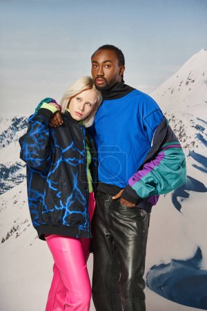 Schönes junges Paar in warmen Outfits, das sich liebevoll vor Bergkulisse umarmt, Winterkonzept