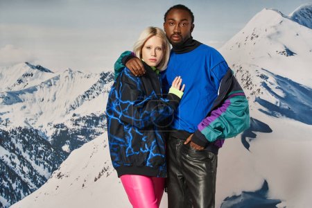 pareja interracial atractiva en trajes elegantes abrazando y mirando a la cámara, concepto de invierno