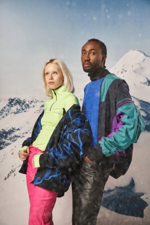 Photo for Attractive diverse couple in stylish warm outfits with snowy mountain on backdrop, winter concept - Royalty Free Image