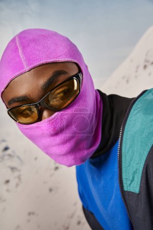 portrait of young stylish man in pink warm balaclava mask with snowy background, winter concept