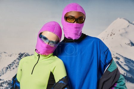 junges stylisches Paar in warmen, lebendigen Outfits und rosa Sturmhauben vor verschneiter Kulisse, Winterkonzept