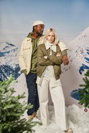 schönes modisches Paar in warmen Winterjacken mit Bergkulisse posiert mit Arm auf Schulter