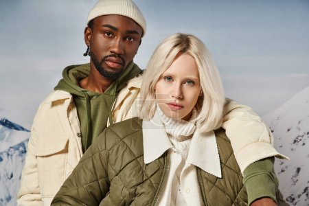 Porträt eines modischen multirassischen Paares in warmer, lebendiger Kleidung, das in die Kamera blickt, Winterkonzept