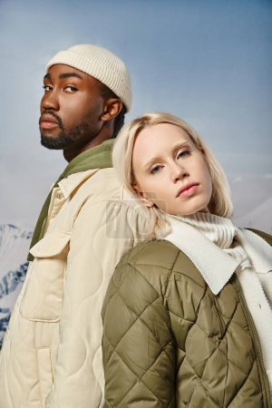 portrait of fashionable couple in warm attire posing back to back looking at camera, winter fashion