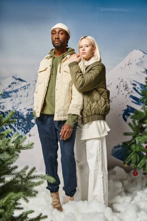 hübsche blonde Frau in warmer Jacke umarmt ihren stilvollen Freund mit Mütze, Wintermode