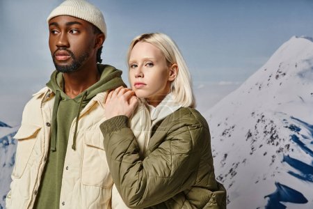 atractiva pareja joven en trajes elegantes con telón de fondo de montaña abrazándose calurosamente, concepto de invierno
