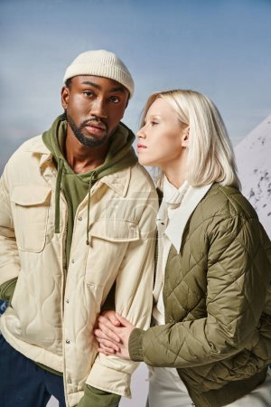 Photo for Beautiful fashionable woman in warm attire holding her stylish boyfriend arm, diverse couple - Royalty Free Image