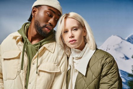 Téléchargez les photos : Couple attrayant dans des tenues modernes élégantes avec montagne enneigée sur fond, concept d'hiver - en image libre de droit