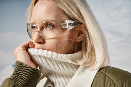 Porträt einer blonden Frau mit Brille, die den Mund mit dem Kragen verdeckt und wegschaut, Winterkonzept