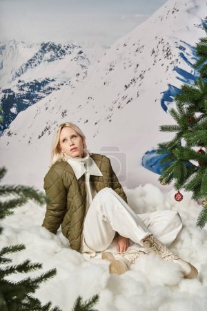 beautiful fashionable woman in stylish attire sitting on snow with crossed legs, winter concept