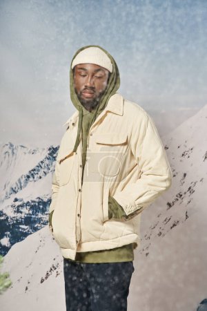 stylischer Mann in trendiger Winterkleidung, der bei Schneefall mit den Händen in den Taschen steht, Mode und Stil
