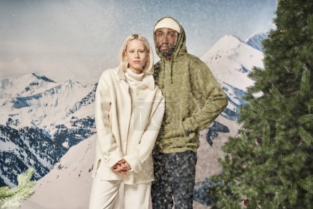 beautiful stylish couple posing together under snowfall in trendy warm jackets, winter concept