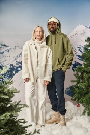 Foto de Hermosa pareja multicultural de pie lado a lado con fondo de montaña, moda de invierno - Imagen libre de derechos