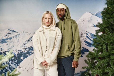 stylish diverse couple in warm trendy jackets posing and looking at camera, winter concept