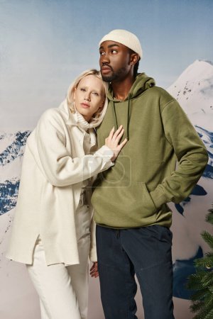 mujer rubia joven con la mano en el pecho de su novio con fondo nevado, moda de invierno