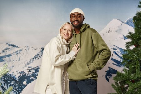happy blonde woman hugging with african american boyfriend with mountain backdrop, winter fashion