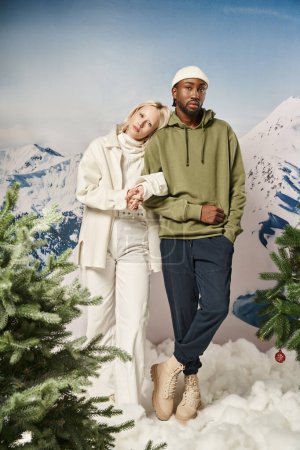 longueur totale de couple interracial élégant en tenue d'hiver debout avec toile de fond de montagne
