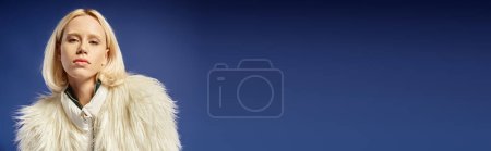 winter banner, portrait of young woman in white faux fur jacket looking at camera on blue backdrop