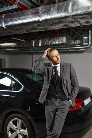 schöner Profi im eleganten schicken Anzug posiert in der Nähe seines Autos auf einem Parkplatz und schaut weg