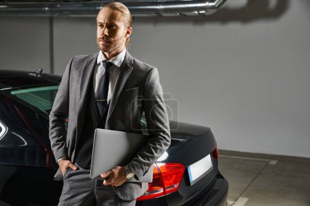 attraktiver Profi im schicken Anzug vor seinem Auto, der wegschaut, Geschäftskonzept