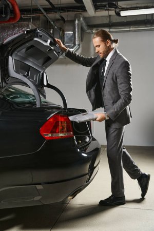 gut aussehender Profi im eleganten Anzug mit Pferdeschwanz verschließendem Kofferraum seines Autos, Geschäftskonzept