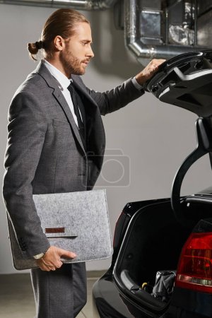Foto de Tiro vertical del hombre guapo con cola de caballo en traje limpio cierre tronco de su coche, concepto de negocio - Imagen libre de derechos
