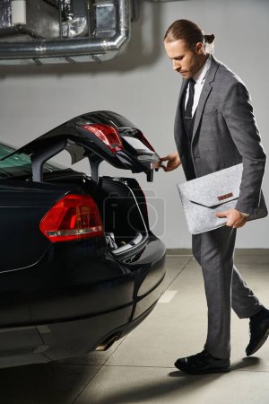 schöner rothaariger Mann im eleganten Anzug, der den Kofferraum seines Autos auf dem Parkplatz schließt, Geschäftskonzept