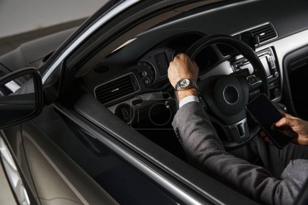 Ausgeschnittene Ansicht eines eleganten Profis mit Armbanduhr im eleganten Anzug hinter dem Lenkrad, Business