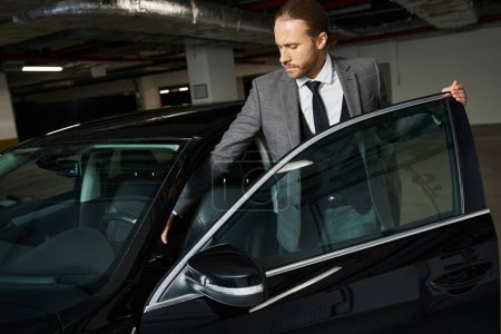 Foto de Atractivo hombre elegante en elegante traje inteligente entrar en su coche en el estacionamiento, concepto de negocio - Imagen libre de derechos