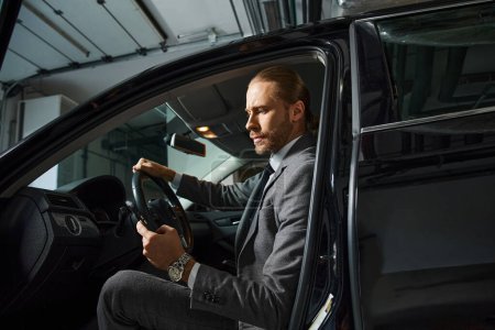 Foto de Hombre barbudo guapo con pelo rojo en traje elegante inteligente detrás del volante de su coche, negocio - Imagen libre de derechos