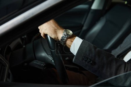Foto de Vista recortada del hombre en traje elegante con reloj de pulsera sentado detrás del volante, concepto de negocio - Imagen libre de derechos