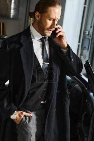 vertikale Aufnahme eines ansprechenden Mannes, der mit der Hand in der Tasche auf dem Parkplatz telefoniert, Geschäftskonzept