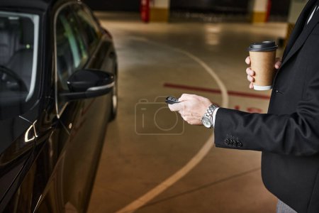vista recortada de hombre elegante en traje negro con taza de café en la mano usando las llaves del coche, concepto de negocio