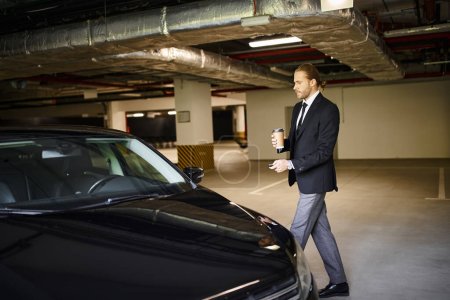 attractive elegant man with beard in black suit holding coffee cup and car keys, business concept