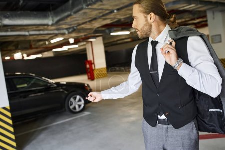 hombre guapo con barba en chaleco negro usando la llave de su coche en el estacionamiento, concepto de negocio