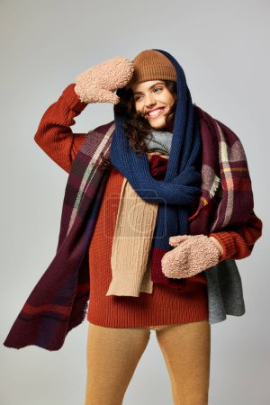 estilo de invierno, mujer joven feliz en capas de ropa, sombrero caliente y bufandas posando sobre fondo gris