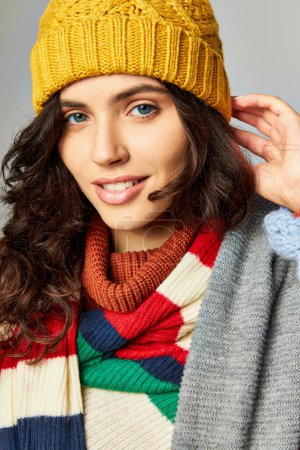 Porträt einer glücklichen Frau mit lockigem Haar in Hut und kuscheligem Pullover mit gestreiftem Schal