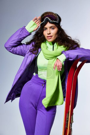 winter activity, attractive woman with curly hair posing in active wear with puffer jacket and skis